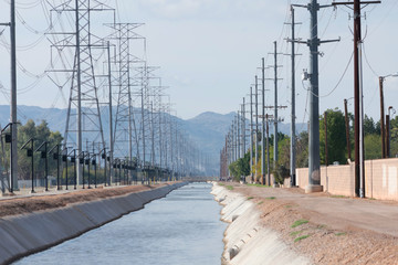 Power lines on both sides of a canal and mountains in the background