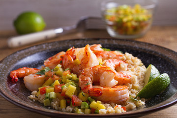 Shrimps with mango avocado and red pepper salsa on cauliflower rice in bowl on wooden table