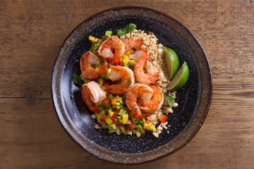 Shrimps with mango avocado and red pepper salsa on cauliflower rice in bowl on wooden table. View from above, top studio shot