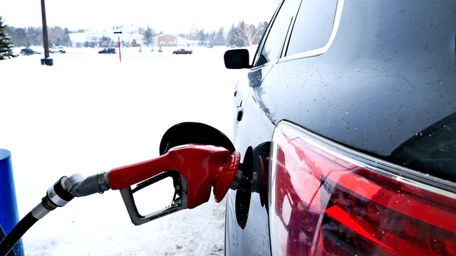 Fuel Nozzle With Red Handle, Filling Gas Tank Of Black Car During Winter Snow Storm In Minnesota.