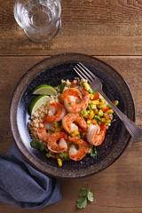 Shrimps with mango avocado and red pepper salsa on cauliflower rice in bowl on wooden table. View from above, top studio shot