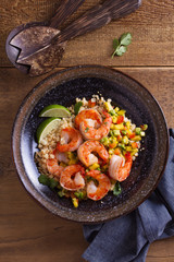 Shrimps with mango avocado and red pepper salsa on cauliflower rice in bowl on wooden table. View from above, top studio shot