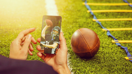 Man use mobile phone, blur image of football match as background.