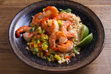Shrimps with mango avocado and red pepper salsa on cauliflower rice in bowl on wooden table