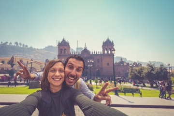 handsome happy tourist couple taking selfie in Plaza de Armas with Inca fountain, Cathedral and...