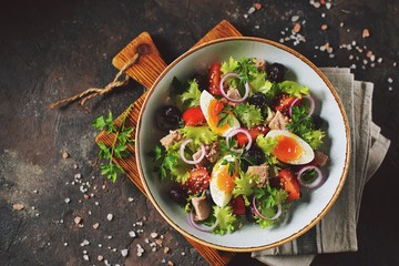Healthy organic lettuce salad with canned tuna, cherry tomatoes, sun-dried olives, red onion, egg and parmesan. Top view. Copy space. 