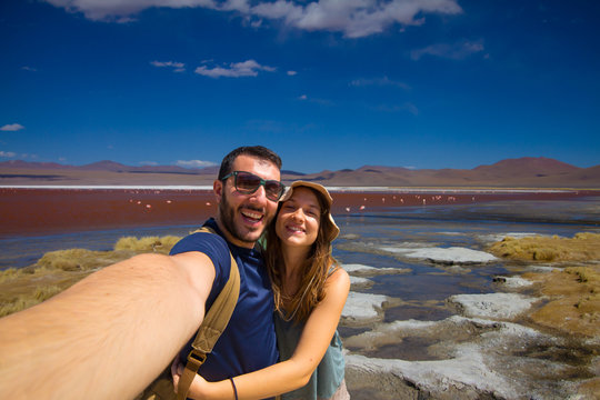 happy tourist couple take selfie photo travelling in the Red Lake, or Laguna Colorada, on the Altiplano near Uyuni inside Eduardo Avaroa National Reserve in Bolivia at 4300 m above sea level.