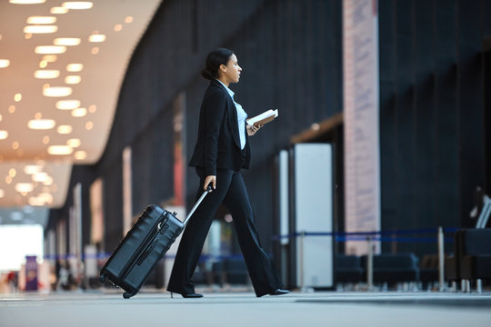 Contemporary business traveler with baggage and tickets walking to exit for airplane