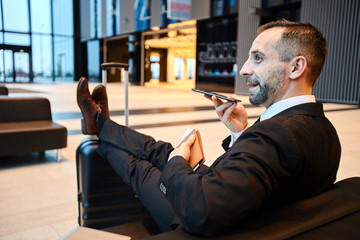 Young mobile businessman using voice messenger while recording message on smartphone in airport...