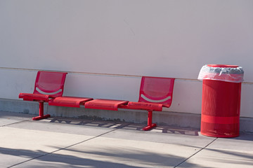 Red metal bench set and garbage can outside a building