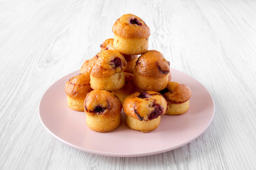 Homemade muffins with cherry on pink plate over white wooden background, side view. Close-up.