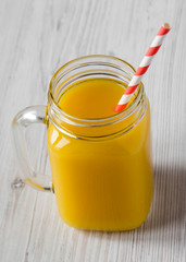 Fresh orange juice in glass jar over white wooden surface, low angle view. Close-up.