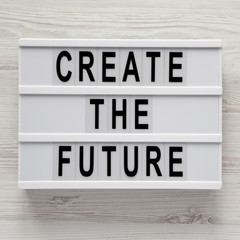 Obraz premium 'Create the future' word on lightbox on a white wooden table, top view. From above, flat lay, overhead.