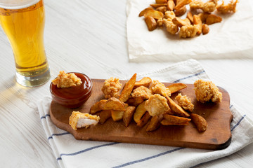 Fried potato wedges, chicken bites, barbecue sauce and glass of beer on a white wooden background, low angle view.