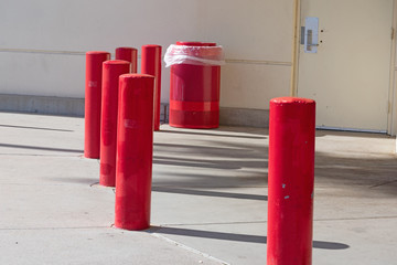 Red painted concrete poles and matching garbage can near a building