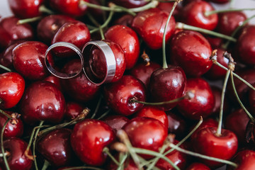 Precious white gold wedding rings lying on fresh useful sweet red cherry