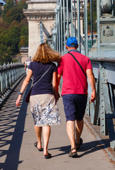 Back silhouette of a couple walking holding hands on a bridge.