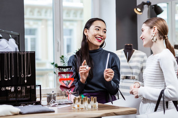 Dark-haired smiling asian woman in a navy polo neck presenting a new fragrance