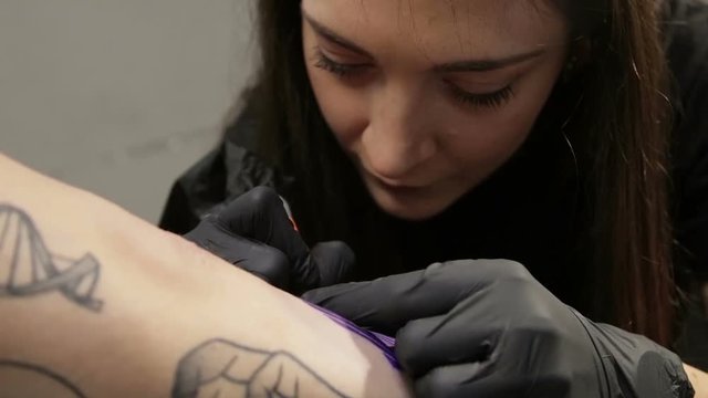 Female tattoo artist focused on her work. Tattooing her client