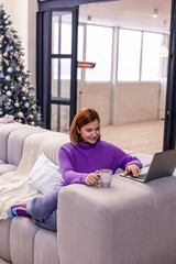 Pretty young red-haired beaming girl in a violet sweater sitting on the sofa