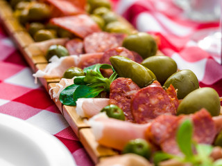 Tapas with salami, ham, cheese and black olives, green olives on a light pattern Scottish tartan napkin. Close-up. An appetizer or snack in Spanish cuisine in Spain.