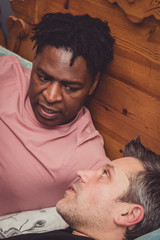 Fototapeta premium An interracial gay couple talking, lying down in their bedroom. 