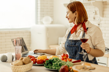 Red-haired young girl with a glass of wine looking at new models online