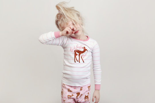 Healthy Sleep Concept. Cute Blonde Caucasian Girl Child In Pink Pajamas With Closed Eyes Pretending Sleeping In Studio Standing Against White Background. 