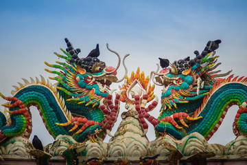 Beautiful two large grimace dragons crawling on decorative tiles roof in Chinese temple. Colorful roof detail of traditional Chinese temple with two dragon on blue sky background.