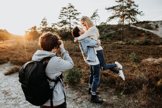 Fotograf schie&szlig;t Foto beim Fotoshooting mit einem verliebten, jungen, gl&uuml;cklichen Paar in der Natur