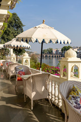 Rattan table and chairs under an umbrella in a street cafe on the shore near the lake in Udaipur, Rajasthan, India.