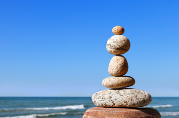 Fototapeta na wymiar Rock zen pyramid of gray pebbles on a background of blue sky and sea.