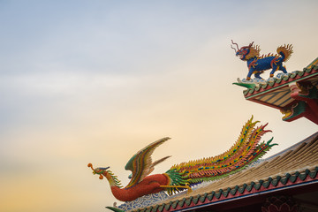 Beautiful Chinese dragon-headed unicorn and Chinese phoenix statues on the roof in Chinese temple with dramatic sky background.