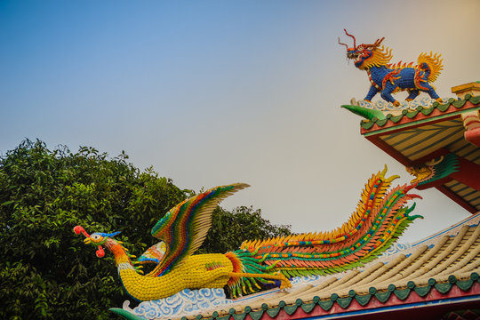 Beautiful Chinese dragon-headed unicorn and Chinese phoenix statues on the roof in Chinese temple with dramatic sky background.