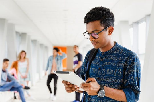A pretty Indian student stands in the university's corridor and reads a notebook