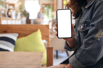Mockup image of a woman holding and showing black mobile phone with blank white screen on the table in modern cafe
