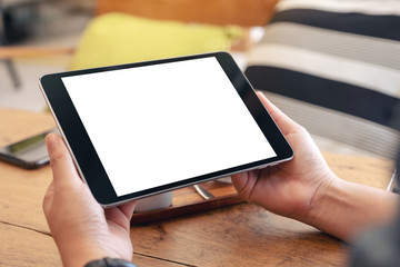 Mockup image of woman's hands holding black tablet pc with blank screen on wooden table in cafe