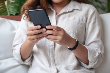Closeup image of a woman holding , using and looking at smart phone in cafe
