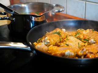 Steaming chicken with Indian curry food in the frying pan. Cooking concept, pieces of chicken fillet in curry sauce ingredients in a pan with the modern kitchen table side view close-up horizontal.