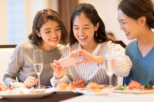 スマートフォンで料理を撮る３人の女性