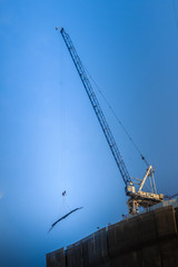View of construction of multi-storey residential building. Condominium under construction with the luffing jib crane. High-rise skyscraper building construction site with crane against bright blue sky