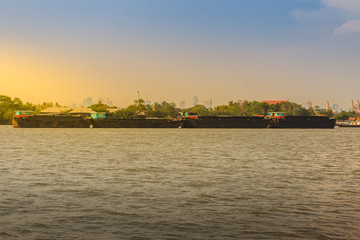 Small tugboat is pulling a large shipping barge up the Chao Phraya River in Bangkok, Thailand.
