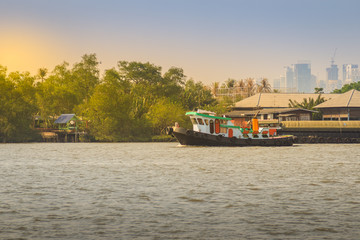 Small tugboat is pulling a large shipping barge up the Chao Phraya River in Bangkok, Thailand.