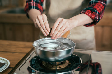 focus on female hands putting pieces chocolate in bowl middle of pot with water on stove cooking cocoa. woman prepare handmade gift dessert on valentine day for lover husband in kitchen alone.