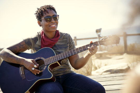 Woman Playing Guitar and Smiling at Friend Outdoors