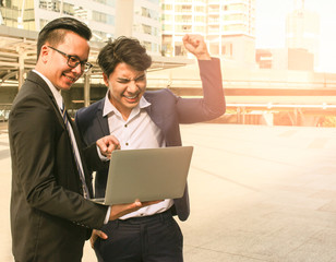 Great job ,two young asian business man keeping arms raise celebrating success in working teamwork concept with laptop