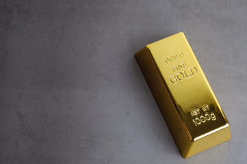 An ingot of gold metal bullion of pure brilliant diagonally located on a gray textured background.