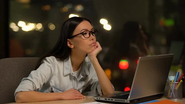 Young woman bored working on laptop in office, lacking motivation, unloved job