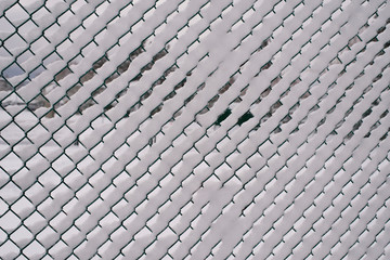 snow filling the holes in a chain link fence..