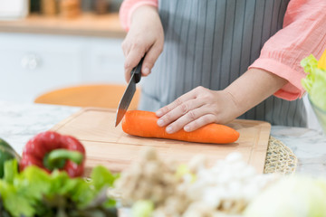 Hand with knife cutting carrot. Woman prepares food at table. Chef cooks delicious dinner. Work that requires skill..